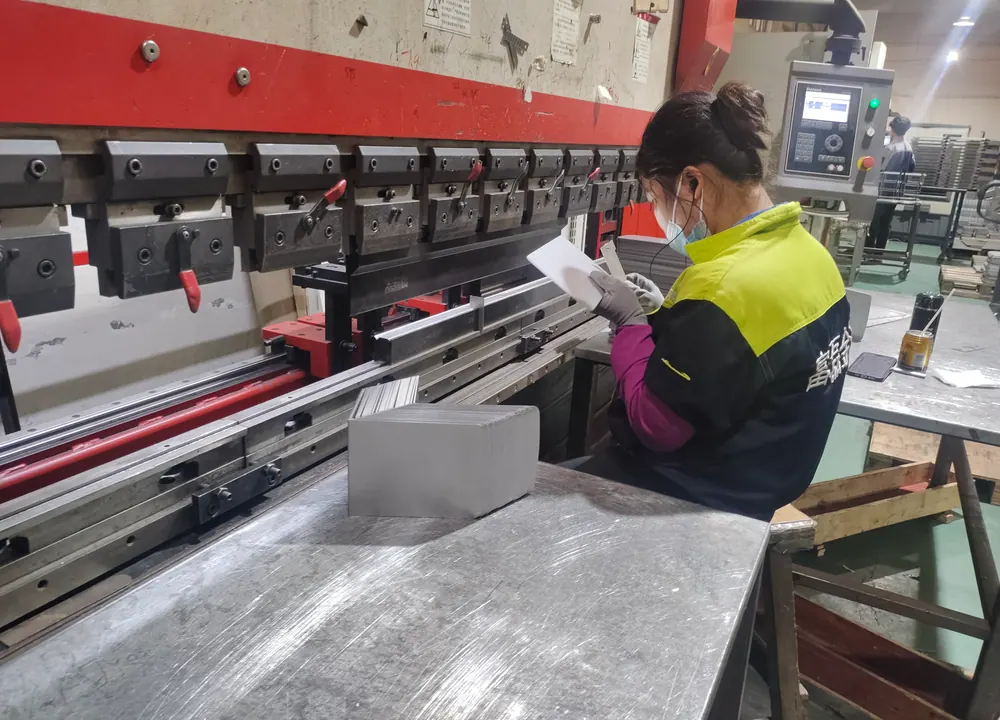 Operator reviewing a drawing and checking a formed sheet metal part at a press brake