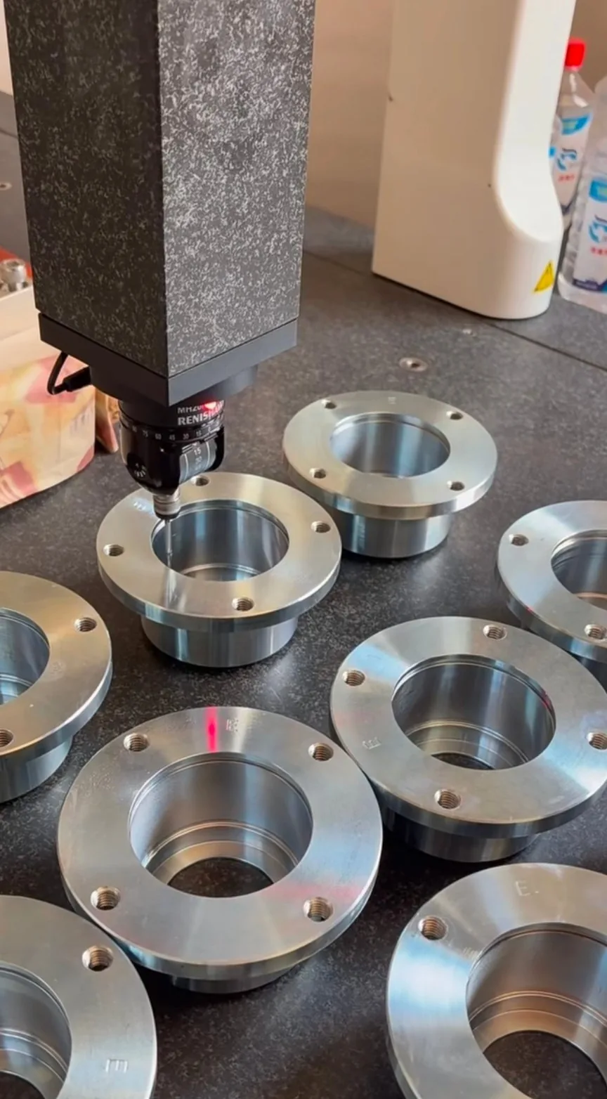 CMM touch probe measuring batch-machined stainless steel flanges in a temperature-controlled inspection room