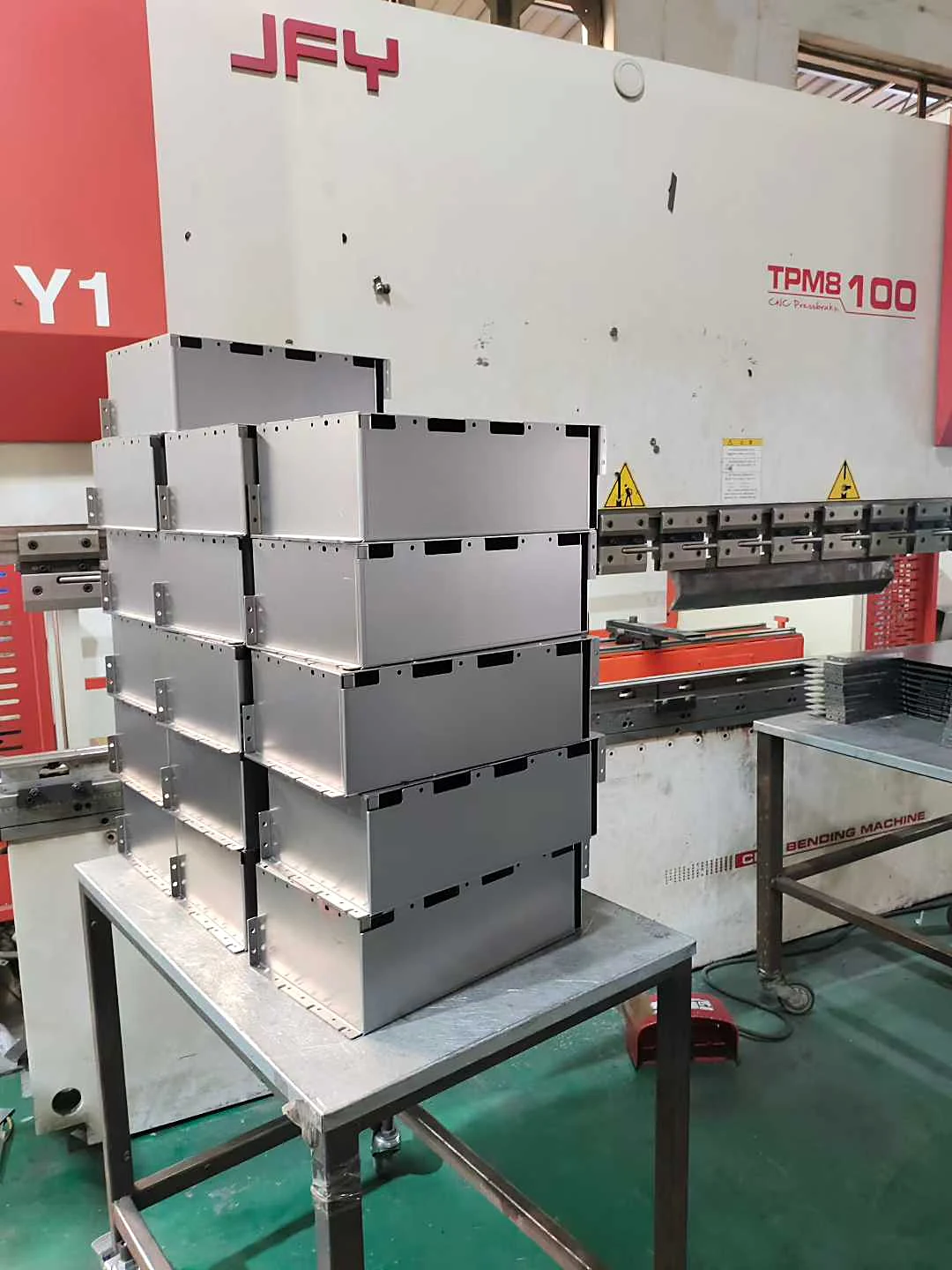 White powder-coated equipment enclosures stacked beside a CNC press brake in the workshop