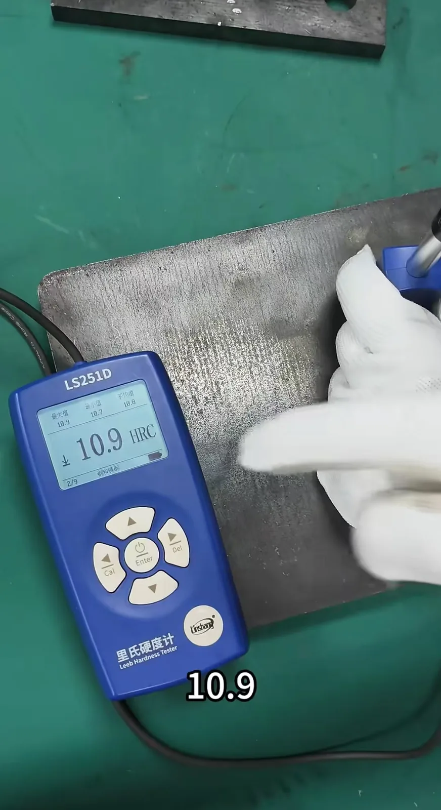 Leeb hardness tester reading being taken on a steel plate by a gloved operator