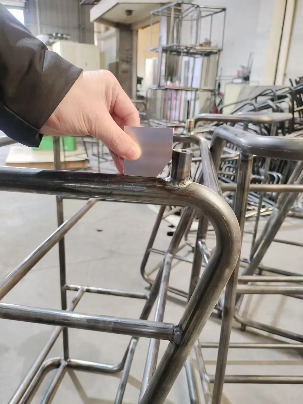 A welded cart frame being checked for square and leg position against the drawing, on the shop floor before surface treatment.